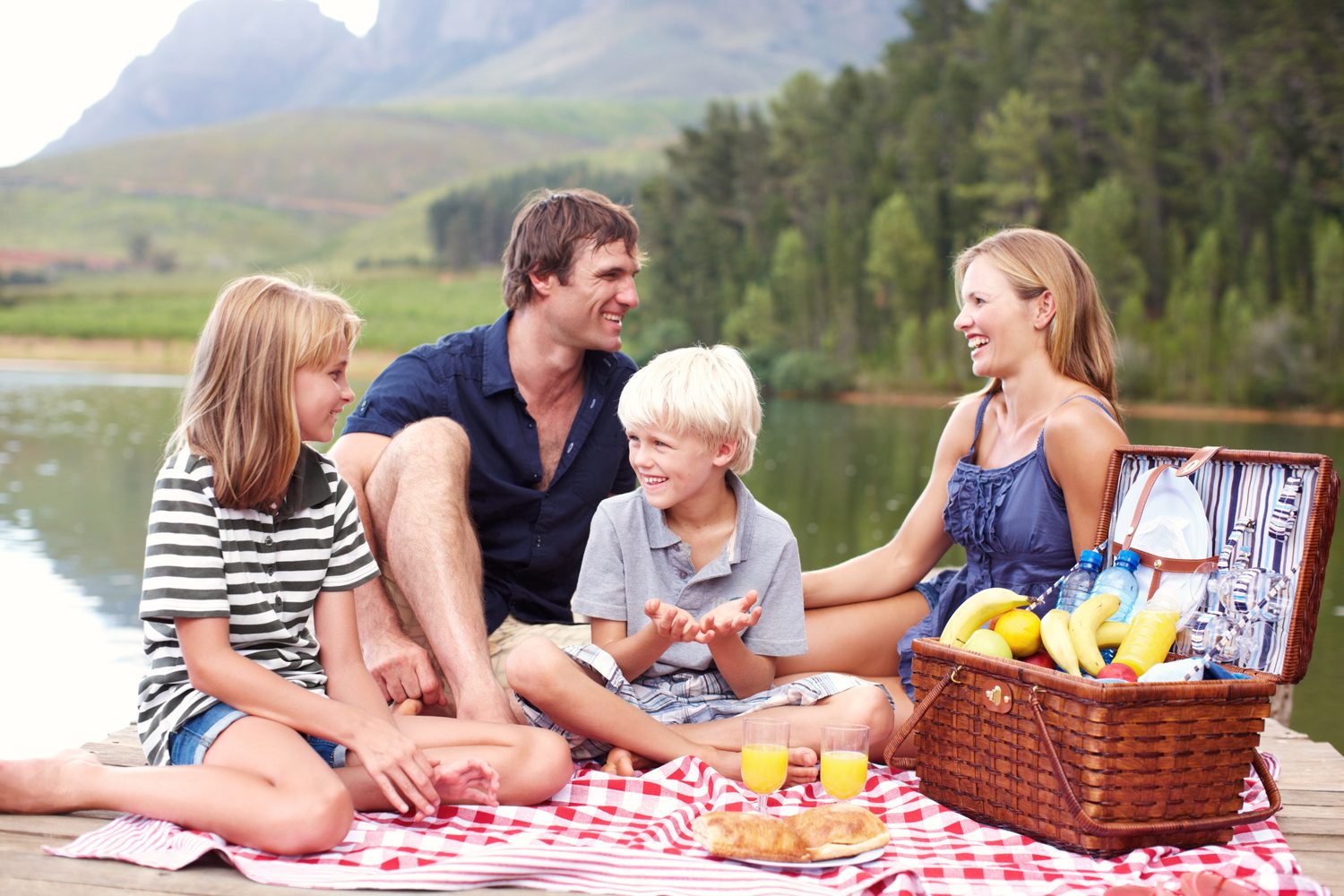 Panier de pique-nique familial posé sur une couverture avec vaisselle réutilisable, gourdes et serviettes.