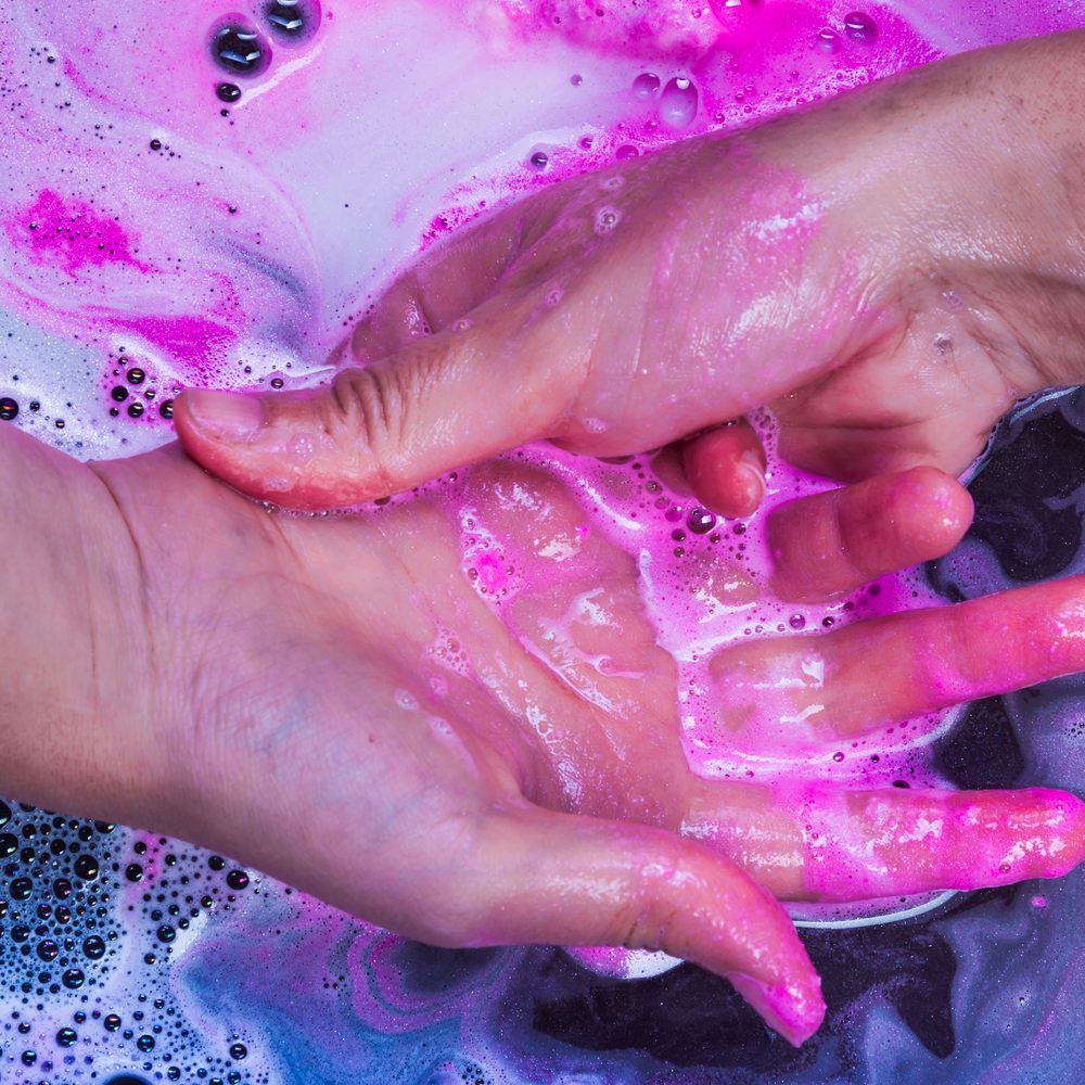 Flacon de shampoing violet utilisé sur une chevelure blonde pour neutraliser les reflets jaunes.